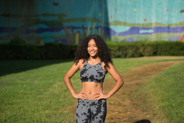 Obraz premium Latina woman, young, beautiful, brunette, with curly hair and sport clothes, with her hands on her waist, happy and content after having completed her exercise routine. Concept sport, exercise.