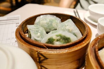A bamboo steamer of spinach dumplings (bor choy gow) at The Eight, a yumcha restaurant at Sydney Chinatown; bamboo steamers of seafood dumplings, and a pot of tea in the foreground