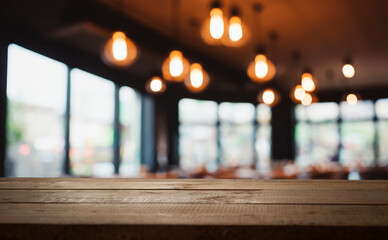 Empty wooden table in a cafe with soft lighting and blurred background.