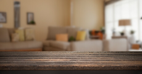 Empty wooden table top with blurred background of a living room with a couch, lamp, and window.