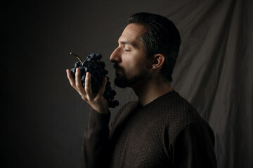 Portrait of a man with grapes in his hands on a gray background