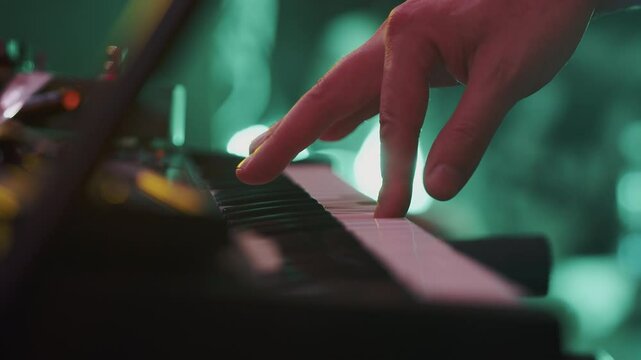 Keyboardist touching and holding the synthesizer keys while playing an inspiring song during the music performance under concert lights close up