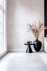 Elegant indoor corner featuring a stylish black side table, a large vase with dried plants, and natural light from a window