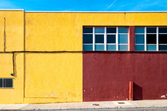 The photo captures the striking contrast of a building's yellow and maroon walls against a clear blue sky, showcasing the fusion of urban settings and artistic elements.