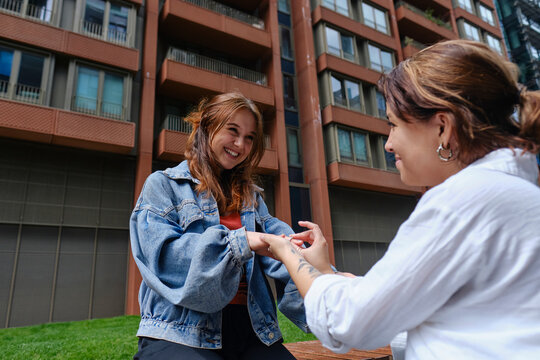 Smiling woman proposing with ring to girlfriend in front of building