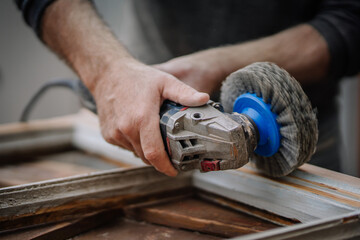 Close-up of a man’s hands using a power sander to smooth a wooden window frame. The image captures the details of the tool and manual work..