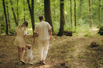 Child embrace parents happiness playing in green grass in park. Happy mother, father hug baby son walking in garden at sunset. Family spending time together outdoors. Children's day. Friendly family.