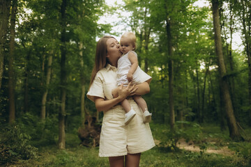 A mother holds her young child in her arms, looking up at something in the distance, as they walk through a forest of vibrant autumn foliage.