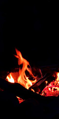 Outdoor campfire. Campfire for cooking food on a camping trip. Fire on a black background. Vertical photo