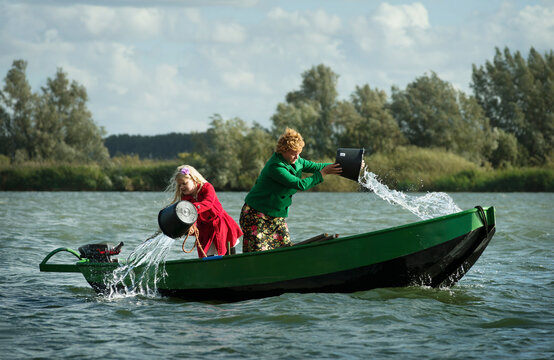 Mother and daughter removing water from leaking boat in lake