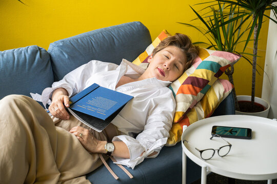 Mature woman sleeping with flight mode symbol on smart phone in living room at home