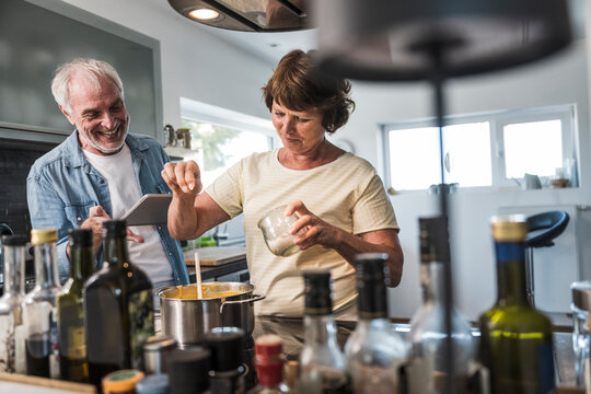 Senior woman standing near man and adding salt in food at home