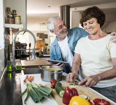Senior man with arm around woman cutting vegetables in kitchen at home