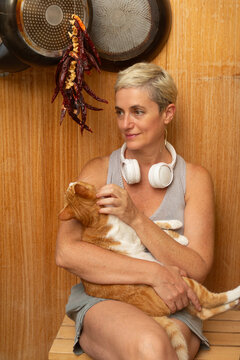 Mature woman sitting with cat in front of wooden wall at home