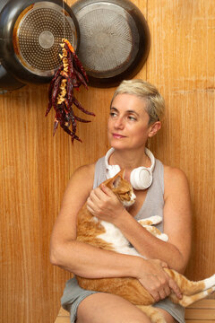 Mature woman holding cat and sitting in front of wooden wall at home