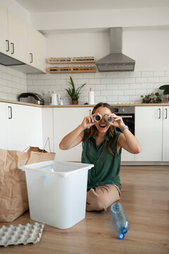 Playful woman imitating binocular with toiler paper roll sitting in kitchen at home