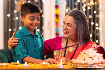 Grandmother and grandson lighting diyas at home during 