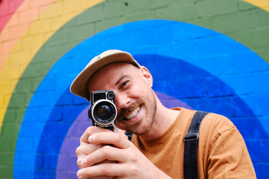 Gay person holding camera near rainbow wall