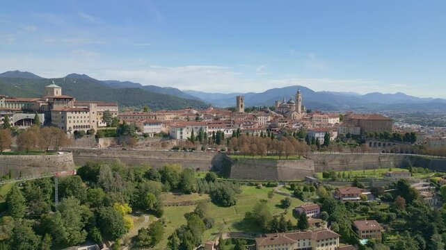 Rapid approach to the medieval city of Bergamo Alta nestled on the green hills, near Orio al Serio Airport during a beautiful sunny day