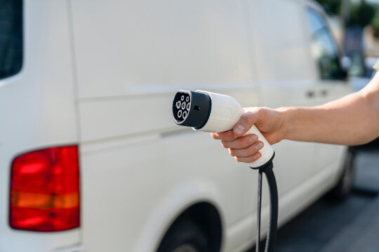 Hand of delivery man holding electric plug near white van at street