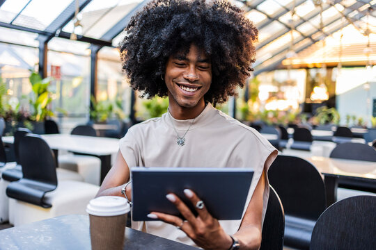 Smiling young man with curly hair using tablet PC at cafe - Powered by Adobe