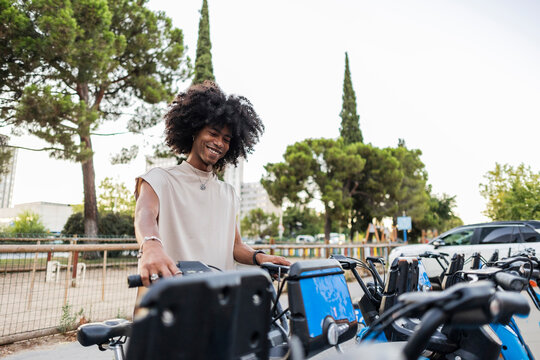 Smiling young man holding electric bicycle at parking station city
