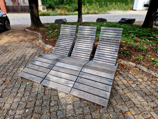 rocking chair on the pavement under the trees in the square. wooden deck chairs made of tropical wood for one person in the park. They are comfortable made of brown planks, slats steel frames, teak