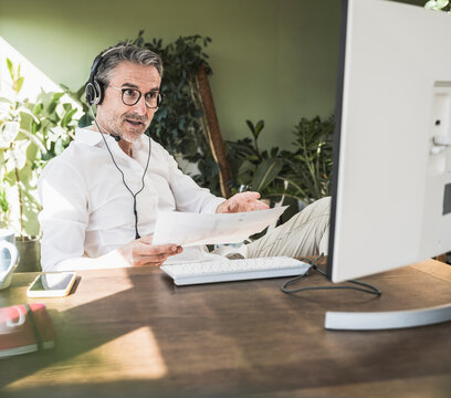 Freelancer with document doing video call sitting at desk in home office
