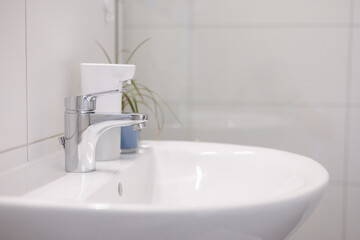Bathroom interior with sink and faucet. White tile and sensor dispenser.