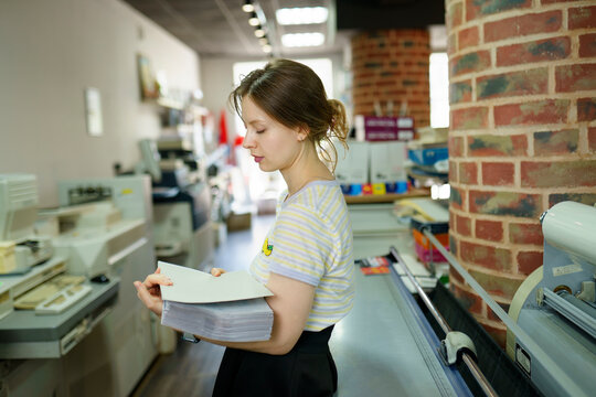 Woman holding stack of papers and standing in a printing shop