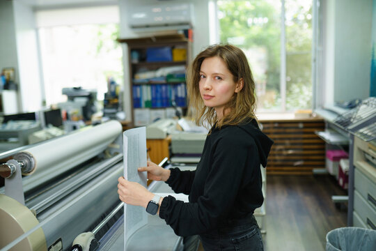 Operator holding documents and standing near large format printer