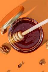 Glass jar full of honey and wooden dipper with honey drop isolated on orange background