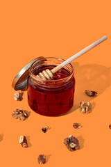 Glass jar full of honey and wooden dipper with honey drop isolated on orange background