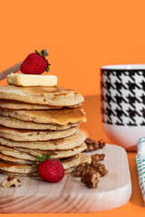 Hand pouring sweet honey onto tasty pancakes on orange background