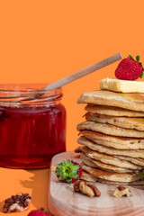 Hand pouring sweet honey onto tasty pancakes on orange background
