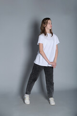 A young girl in casual wear stands with a gentle tilt, her hands loosely clasped in front of her....