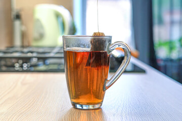 Freshly brewed tea is gently steaming in a clear glass cup on the kitchen counter