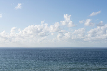 Fototapeta premium The horizon view of the sea and fluffy white clouds, against a bright blue sky, with little editing.