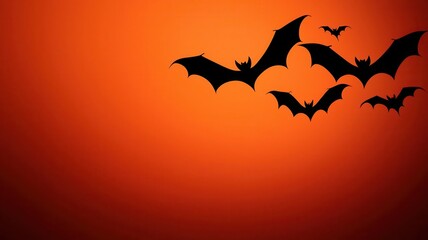 Fototapeta premium Silhouettes of bats flying against a vibrant orange sunset, creating a spooky and atmospheric Halloween scene.