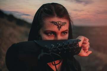 Beautiful girl in black gothic style clothes with tattoo on her face