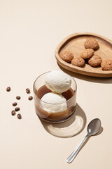 Affogato coffee with vanilla ice cream scoops and espresso in a glass on a yellow background with coffee beans amaretti cookies and shadow.