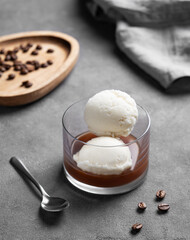 Affogato coffee with vanilla ice cream scoops and espresso in a glass on a dark background with coffee beans and spoon.