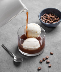 Affogato coffee with vanilla ice cream scoops and espresso poured into a glass on a dark background with coffee beans and spoon.