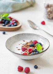 Granola with yogurt, raspberry and blueberries in a bowl on a light background close up. Concept of healthy breakfast