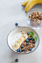 Granola with yogurt, banana and blueberries in a bowl on a white background with morning light.
