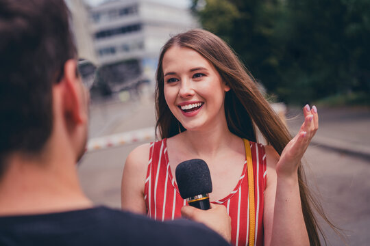 Photo of charming girl giving interview to journalist speaking in microphone broadcast outdoors