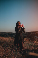 Beautiful girl in gothic style clothes with tattoo on her face plays ocarina in the mountains