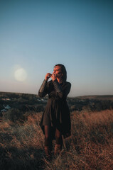 Beautiful girl in gothic style clothes with tattoo on her face plays ocarina in the mountains