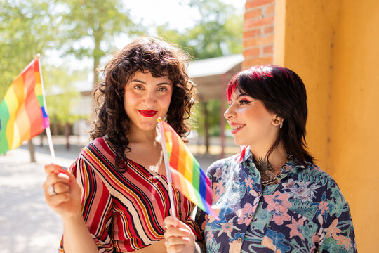 Joyful lesbian couple with pride flag in sunny park