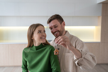 Family happily embraces with keys with house in hand after moving into new apartment. Couple look...